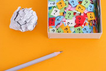 Pencil with crumpled paper ball and question marks in a paper box on yellow background
