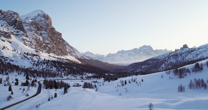 Forward aerial to snowy valley with woods forest and road at falzarego pass.Sunset or sunrise, clear sky.Winter Dolomites Italian Alps mountains outdoor nature establisher.4k drone flight