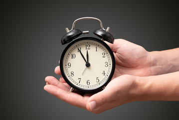 Hand holding clock with five minutes to twelve o'clock