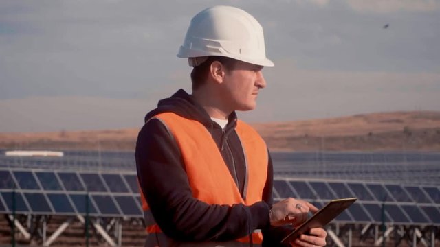 a man in a helmet engineer on the background of a solar power plant holding a digital tablet