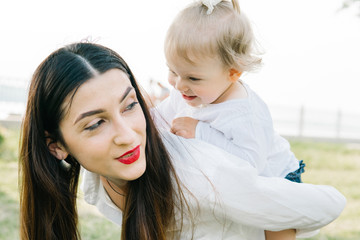  beautiful woman in the park or forest near the trees and holding her smiling little baby girl 