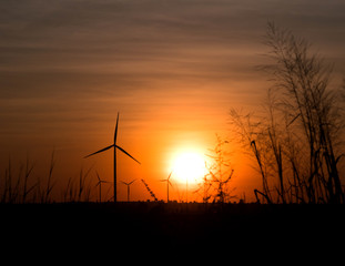 silhouette wind turbine in grass field with twilight and sunset