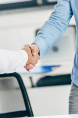 close-up partial view of businessmen shaking hands at workplace