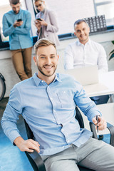 Fototapeta premium handsome young businessman smiling at camera while working with colleagues in office