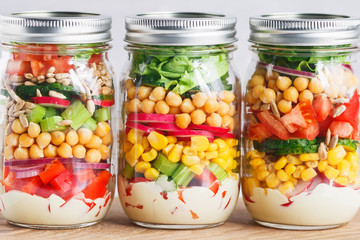 Three glass jars with layering various vegan salads for healthy lunch. The concept of fitness and vegetarian food.