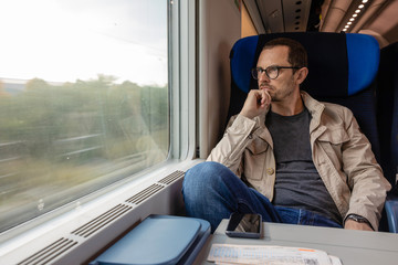 Middle age man looking out of the window of train. Passenger during travel by high speed express...
