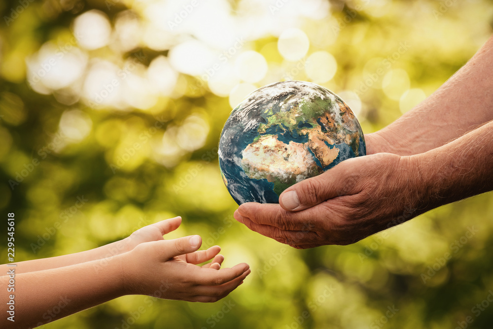 Wall mural close up of senior hands giving small planet earth to a child over defocused green background with c