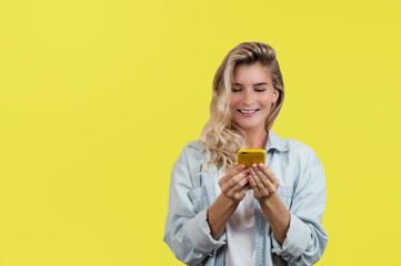 emotional very beautiful young girl looks into the phone and celebrates the victory standing on an isolated yellow background.