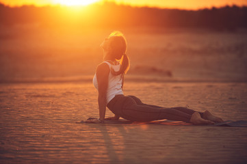 Beautiful young woman practices yoga asana Urdhva Mukha Svanasana - upward facing dog in the desert at sunset
