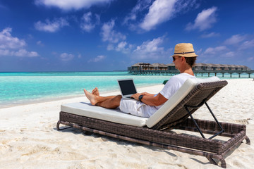 Arbeit im Urlaub: Geschäftsmann mit Laptop auf Liege am tropischen Strand