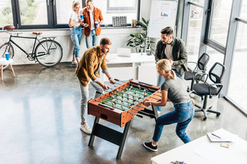 high angle view of young casual business people playing table football at office and having fun...
