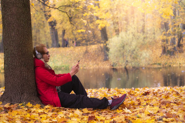 Happy and realax time of Young man with headphone and listening a music of smart phone which sitting on a fallen autumn leaves in a park