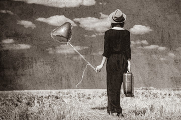 photo of the beautiful young woman with heart-shaped balloon and suitcase in the field