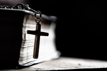 Cross with Bible on a old oak wooden table. Beautiful dark background. Religion concept