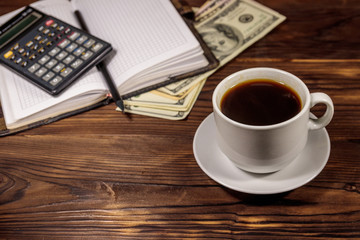 Cup of coffee and notepad with dollars, pencil and calculator on wooden desk. Financial concept