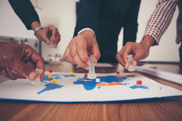 The hand of a group of businessmen holding chess and putting on a map.
