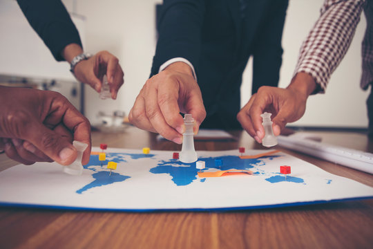 The hand of a group of businessmen holding chess and putting on a map.