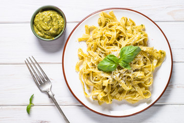 Tagliatelle pasta with pesto sauce and parmesan on white.