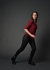 full length portrait of brunette girl wearing  red shirt and leather pants. standing pose, on grey...