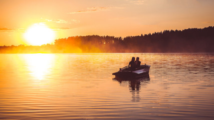 Couple in love ride in a rowing boat on the lake during sunset. Romantic sunset in golden hour. Happy woman and man together relaxing on water nature around