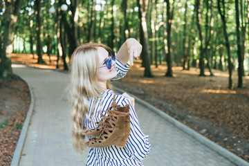 Beautiful portrait of a young teenage girl. long hair. Blonde girl in summer dress. brown shoes in hands