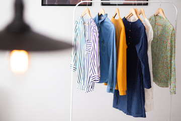 Clothes hang on wooden coat hangers in clothing store with home tone. Shopping and spending concept