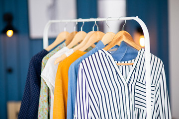 Clothes hang on wooden coat hangers in clothing store with home tone. Shopping and spending concept