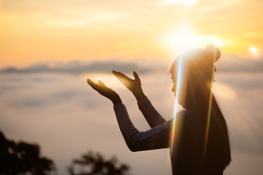 Silhouette of woman praying over beautiful against sunrise background