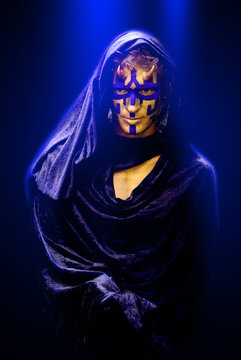 Serious handsome young man with abstract Halloween make up dressed in black like a monk, with blue light coming from above