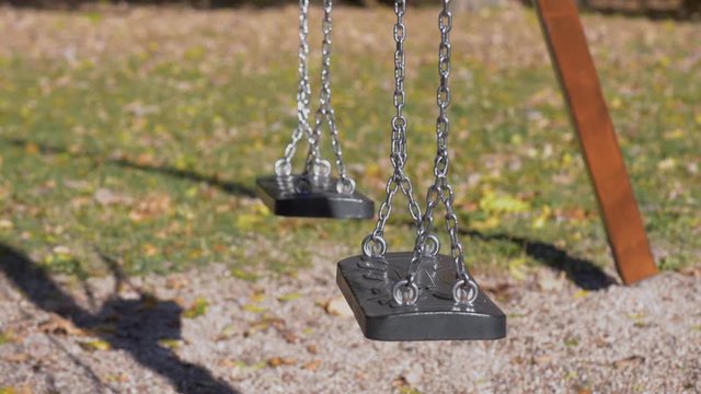 Abandoned empty swings swaying in the wind at children playground outdoors -  in a park an autumn sunny day.