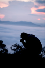 Silhouette of teen girl kneeling and praying over beautiful sunrise background.