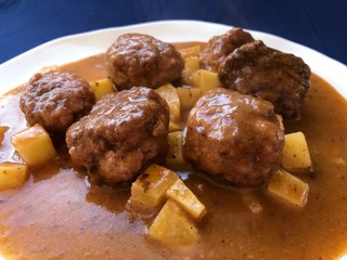 meatballs cooked in sauce of vegetables with a lining of potatoes. Typical Spanish food in white plate and blue background