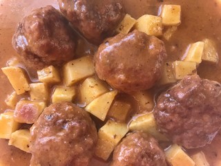 meatballs cooked in sauce of vegetables with a lining of potatoes. Typical Spanish food in white plate and blue background top view