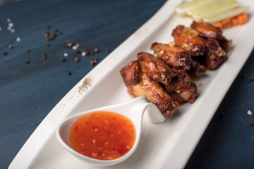 Baked chicken wings with carrots and celery and sweet chili sauce on white plate