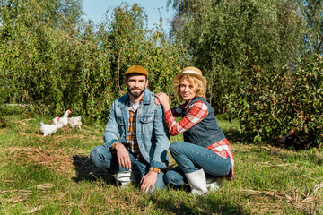 adult farmers sitting on grass and chickens running behind outdoors