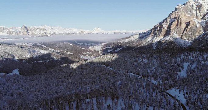 Forward aerial to snowy valley with woods forest and road at Valparola pass.Sunny sunset or sunrise, clear sky.Winter Dolomites Italian Alps mountains outdoor nature establisher.4k drone flight