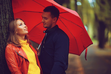 rain in the autumn park / young 25 years old couple man and woman walk under an umbrella in wet...