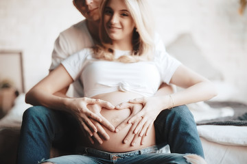 pregnancy concept childbirth and love / man and woman, big belly, hands in the shape of a heart, symbol of pregnancy and love - obrazy, fototapety, plakaty