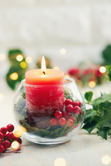 Christmas Table Decoration. Glass vase with holly berries and red candle.