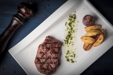 Grilled beef steak with souce, baked potato and onion on white plate with pepper