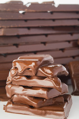 Stack of melting chocolate's pieces with big stack of chocolate on background