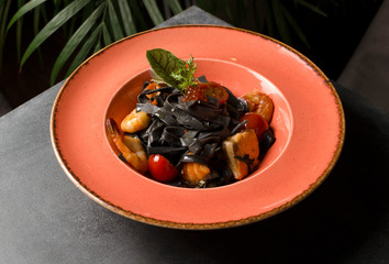 Black tagliatelle with seafood and grilled fish with caviar in an orange plate