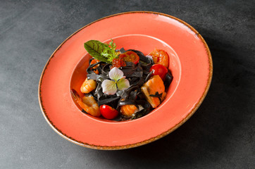 Black tagliatelle with seafood and grilled fish with caviar in an orange plate