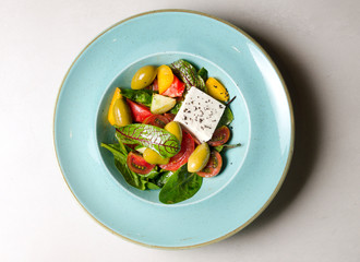 Vegetable salad with feta cheese and large olives on a blue plate