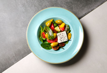 Vegetable salad with feta cheese and large olives on a blue plate
