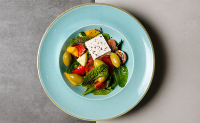 Vegetable salad with feta cheese and large olives on a blue plate