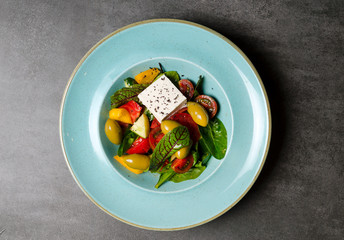 Vegetable salad with feta cheese and large olives on a blue plate