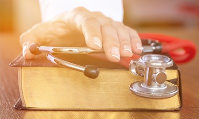 hand with stethoscope on top of old book