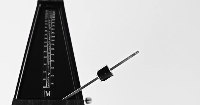 Black and white close-up shot of vintage metronome with pendulum beats slow rhythm on the gray background