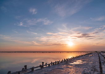 Obraz premium sunset on a pink salt lake, a former mine for the extraction of pink salt. row of wooden pegs overgrown with salt